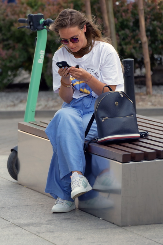 25 - Young woman sitting on a bench using a smartphone